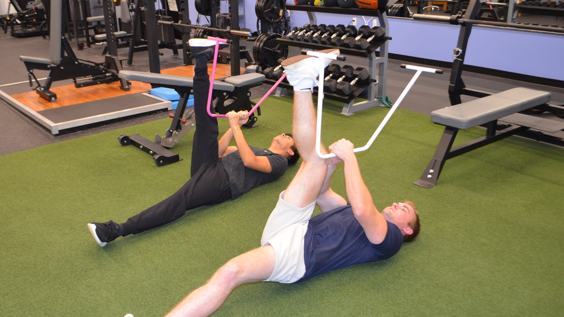Two people performing assisted stretching on a green floor  in a gym setting.